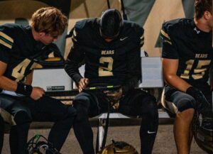 Basha High School football players sit on a bench and watch video replays