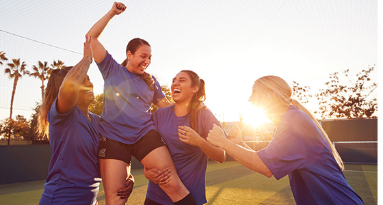 image shows a group of female athletes celebrating and hoisting one athlete in the air