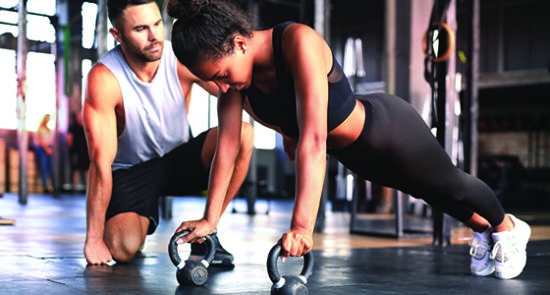 Sporty woman doing push-up in a gym, her coach is watching her