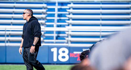 image shows a male coach on a football field looking toward the left