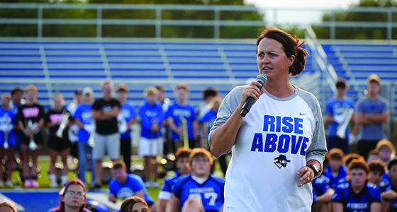 image shows a woman speaking to a crowd on a football field