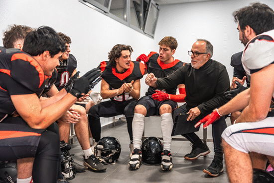 Picture shows a coach giving postgame messages to football players on a bench after the game