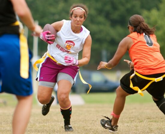 image shows a girls flag football play running with the ball in between two defensive players