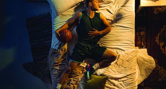 male athlete sleeping on bed with basketball