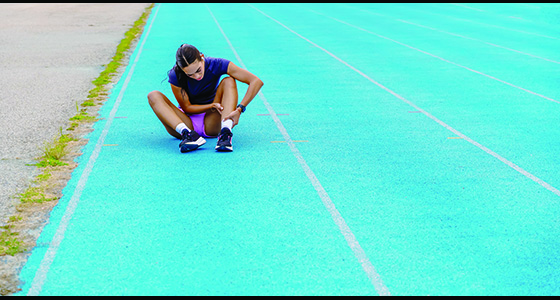 image shows a woman sitting on a running track holding her ankle in pain