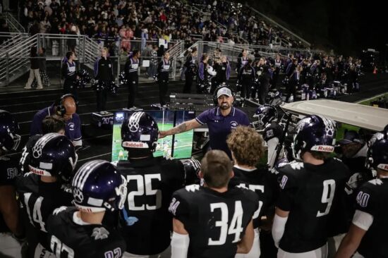 a spanish springs high school football coach points to a video replay screen and talks to a group of high school football players